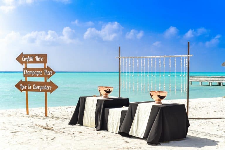 A scenic beach wedding setup with elegant tables and champagne on a sunny day.