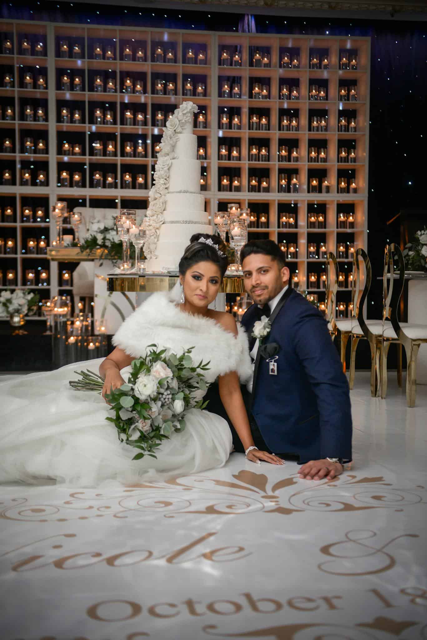 Beautiful couple poses indoors for wedding photoshoot with grand cake display.