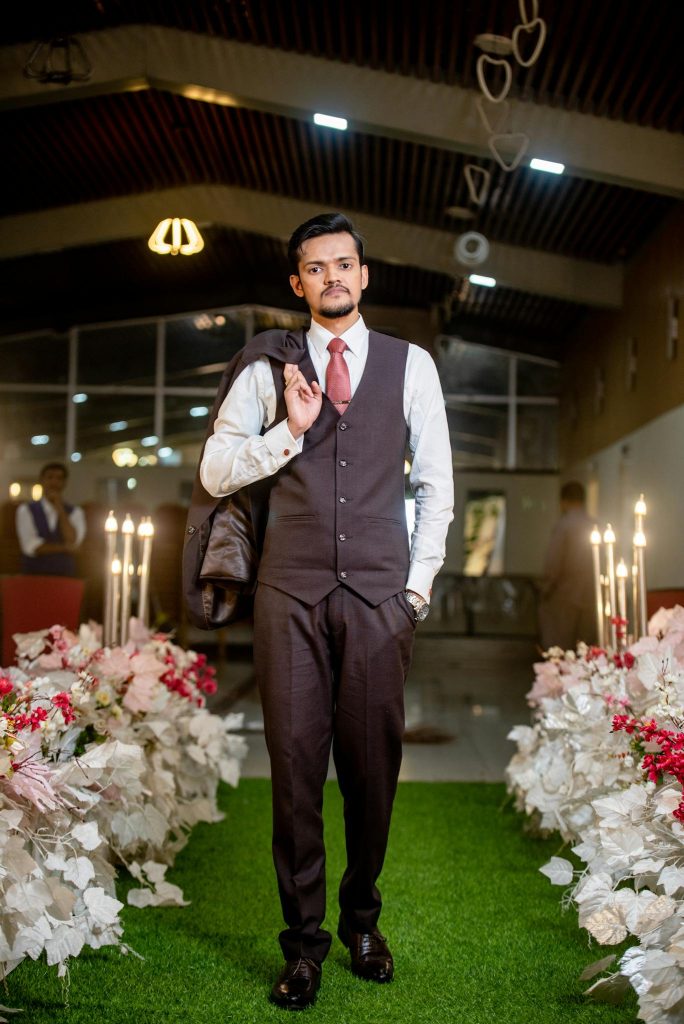 Groom standing in an elegant indoor setting with floral arrangements and candles, dressed in a formal suit.